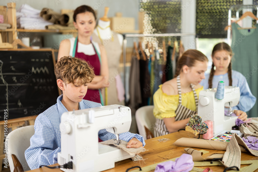 Obraz premium Boy learns to sew on a sewing machine in class as children watch him