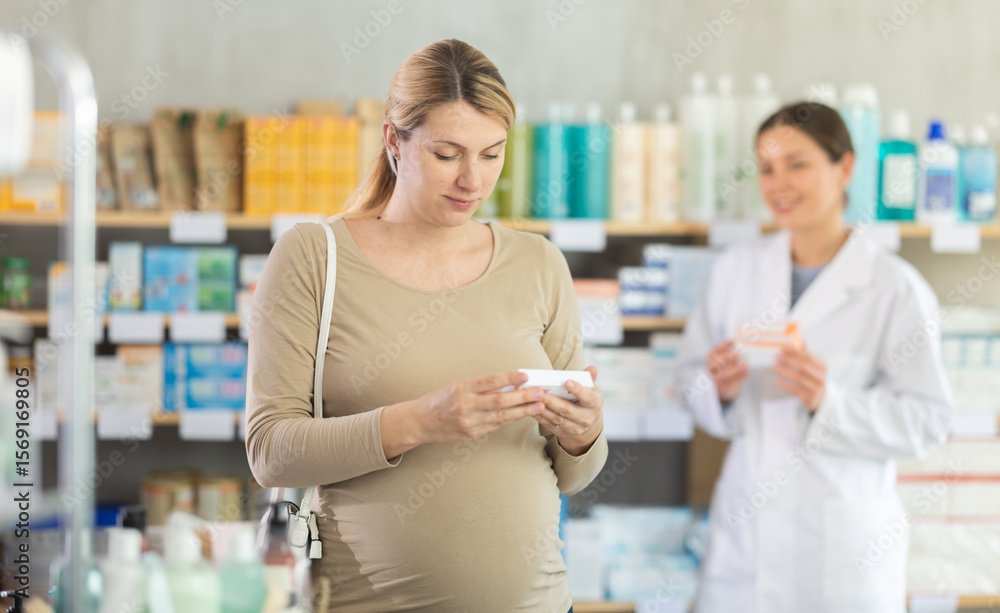 Obraz premium Pregnant woman chooses ointment in pharmacy, examines packaging. Diaper rash remedy, protective diaper cream. Girl pharmacist offers similar product, promotes product of European brand