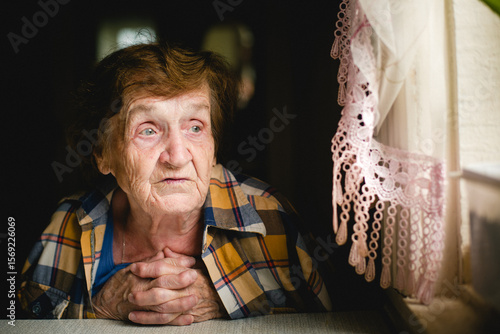 Fotografia An elderly woman, wrapped in a man's shirt draped over her shoulders, gazes thoughtfully out the window
