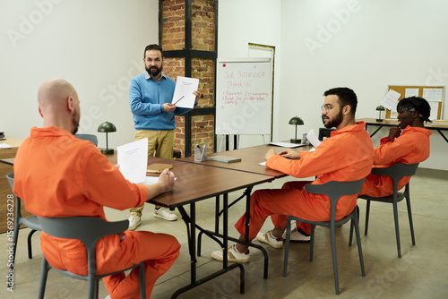 Obraz na plátně Middle aged Caucasian man instructing three multiethnic male prisoners wearing o