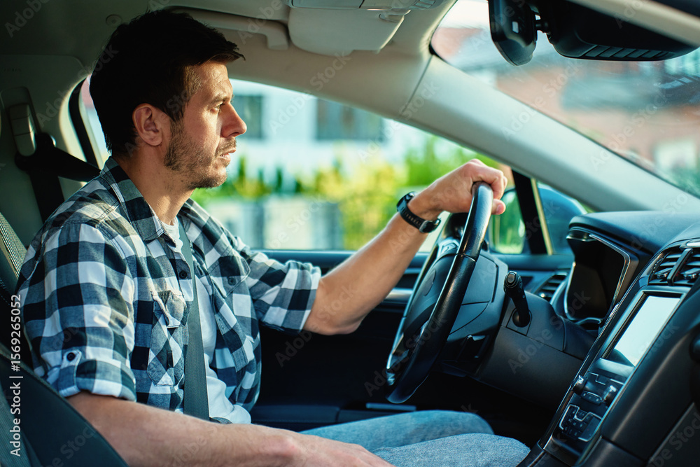 Obraz premium Man driving car and looking ahead with focus, sitting in modern vehicle interior. Concept of daily commute, safe driving and transportation