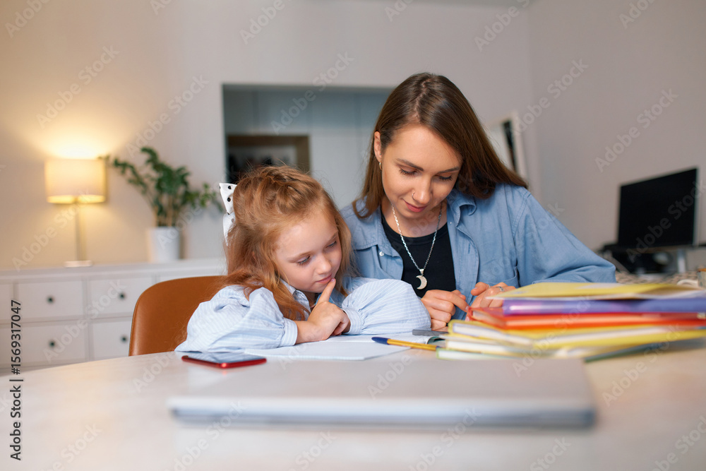 Young mother sits with her child and conducts a school lesson while sitting at her desk Young mother sits with her child and conducts a school lesson while sitting at her desk