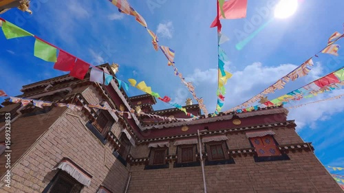 Colorful prayer flags flutter above a traditional stone-and-wood Tibetan-style house—capturing spiritual rhythm, architectural charm, and the interplay of culture and mountain wind in a peaceful ethni