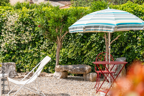 Fotografía Coin détente au jardin avec parasol rayé et banc en pierre rustique