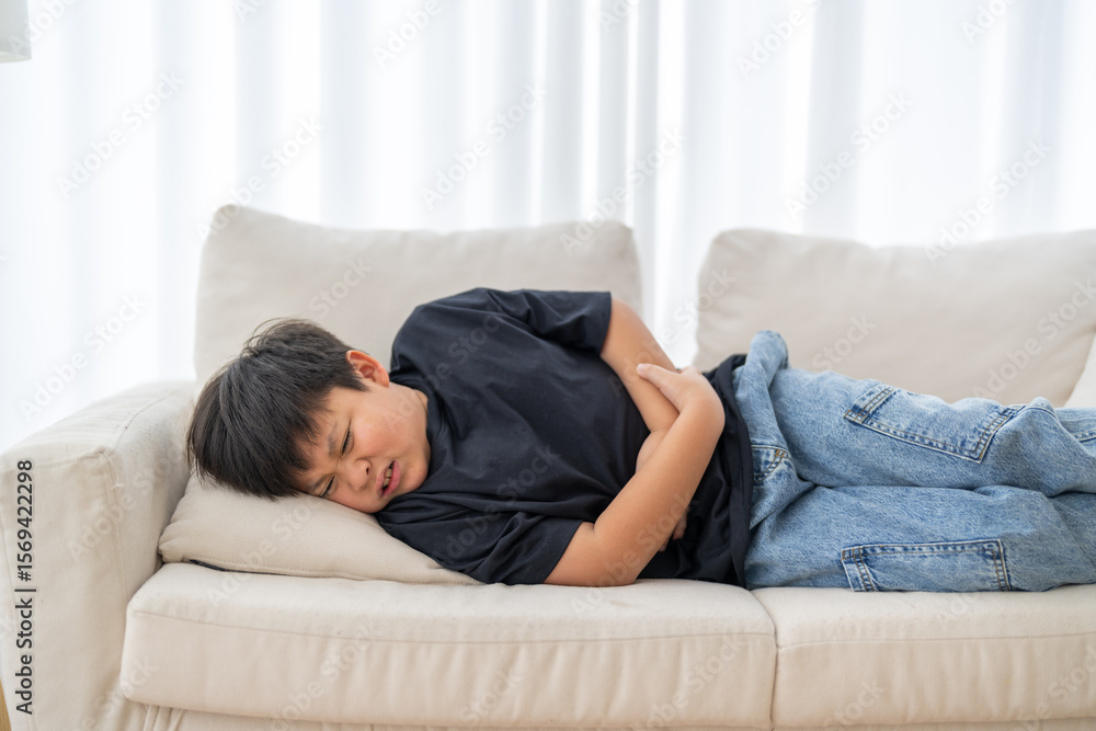Portrait of sick unhappy little child asian boy touching belly stomach with suffering from stomach ache pain, gastritis, gastroenteritis, food poisoning, diarrhea, intestinal inflammation at home Portrait of sick unhappy little child asian boy touching belly stomach with suffering from stomach ache pain, gastritis, gastroenteritis, food poisoning, diarrhea, intestinal inflammation at home