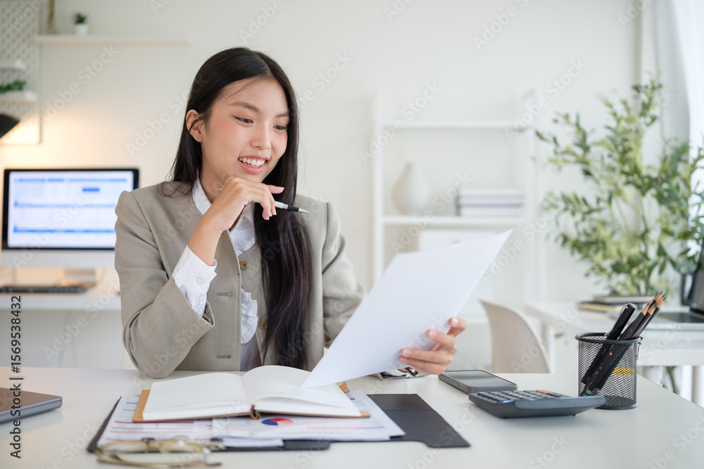 Asian woman in business attire analyzing paperwork and taking notes in a contemporary workspace. Focused on financial and business planning. Asian woman in business attire analyzing paperwork and taking notes in a contemporary workspace. Focused on financial and business planning.