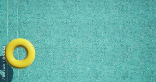 Top view of a bright yellow inflatable ring floating on clear turquoise water in a swimming pool. Sunlight casts a distinct shadow on the mosaic tiles. Minimal, peaceful summer vacation vibe