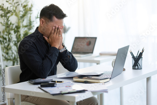 Overworked entrepreneur managing tasks and feeling pressure while working on a laptop in an office.