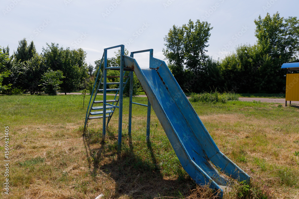 Fototapeta premium A Vibrant Blue Slide in a City Park Surrounded by Greenery Inviting Joy and Playfulness for Children and Families Enjoying the Outdoors on a Sunny Day