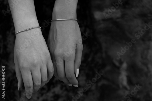 Black and white close-up of two female hands gently touching with matching silver bracelets