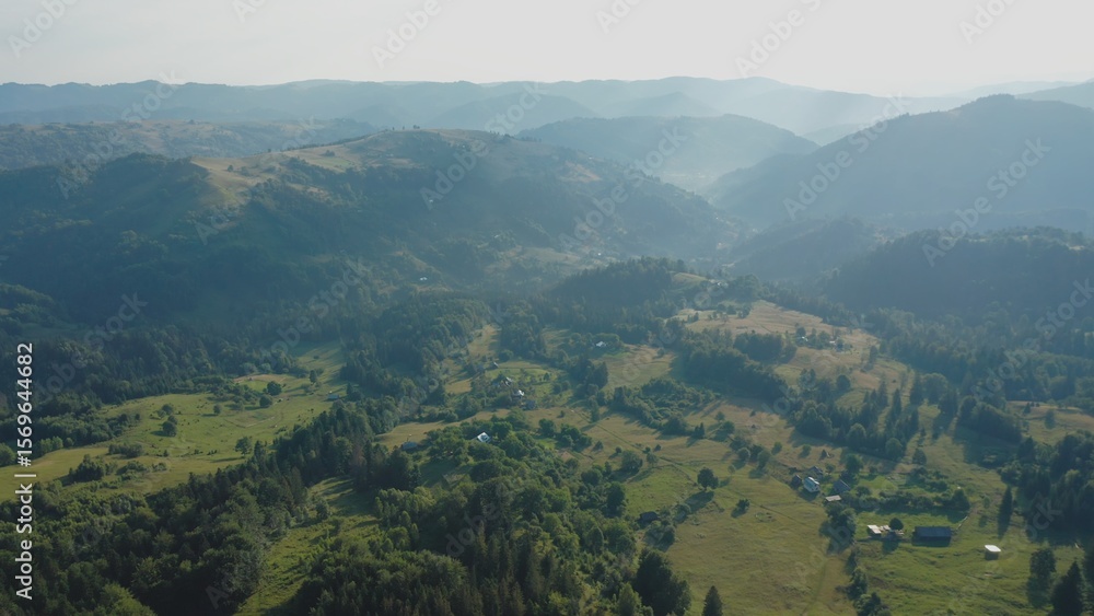 Obraz premium Aerial view of a fog creeping over the mountains surrounding the valley on a summer day.
