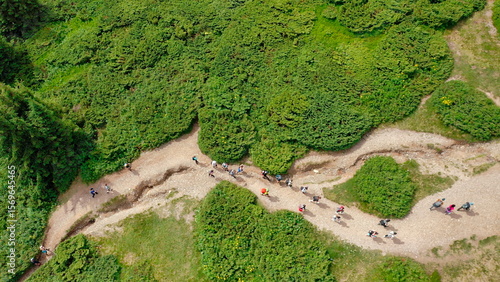 A top-down aerial view of young people walking along a mountain trail to the top of the mountain.