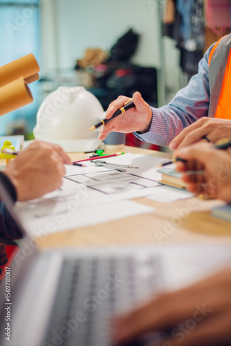 Engineers and architects discuss and consider construction plans for new renewable energy project in office with design documents, laptop and hard hat on table. Concept of engineers and architects+