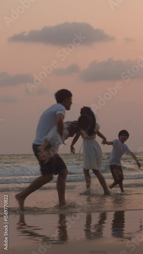 Vertical Screen : Asian young happy family enjoy vacation on beach in evening. Dad, mom and kid relax play together near sea silhouette sunset. Lifestyle travel holiday vacation summer. Slow motion.