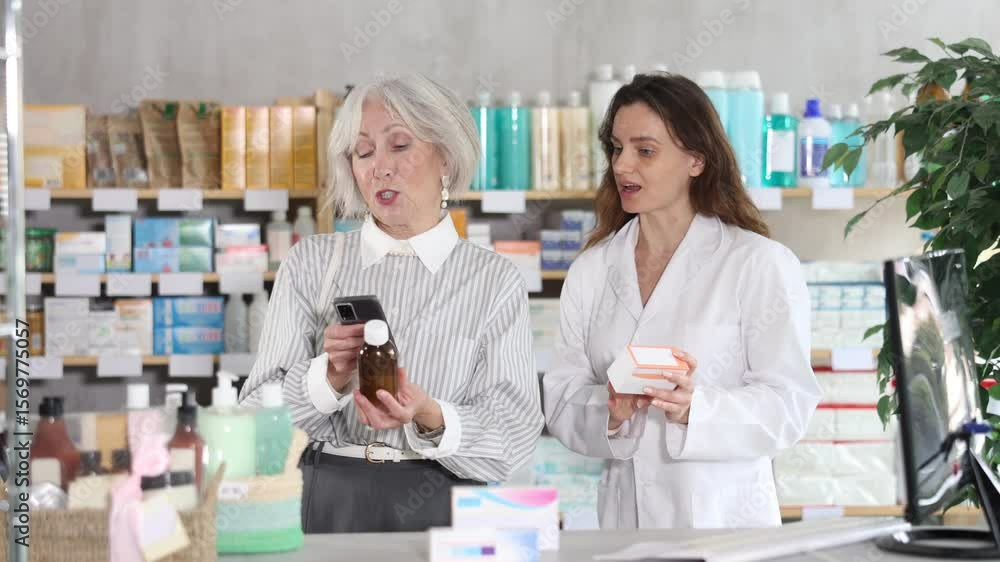 Mature woman in pharmacy scans QR code on expectorant syrup product, checks certificate on manufacturers website and consulting with woman pharmacist about using product Mature woman in pharmacy scans QR code on expectorant syrup product, checks certificate on manufacturers website and consulting with woman pharmacist about using product
