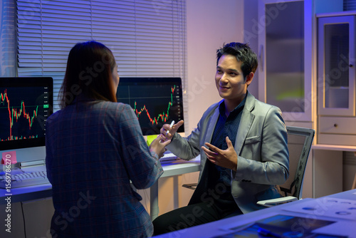 Stockbrokers analyzing graphs on computer screens in office at night