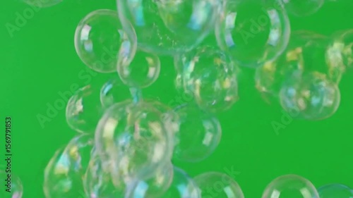 Transparent soap bubbles floating and reflecting light against a vibrant green background.