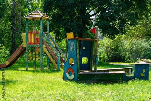 Canvas Print Old abandoned playground among green trees in summer