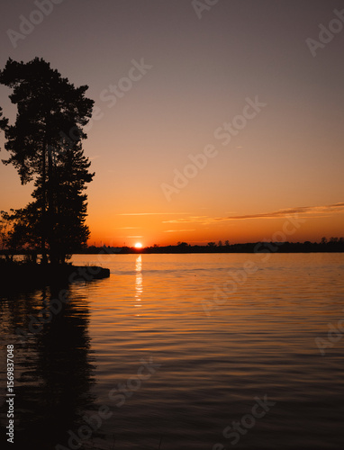 A breathtaking red sunset over a tranquil lake, capturing the serene beauty of nature at dusk. The vibrant hues of crimson, orange, and gold reflect off the still water, creating a mirror-like surface