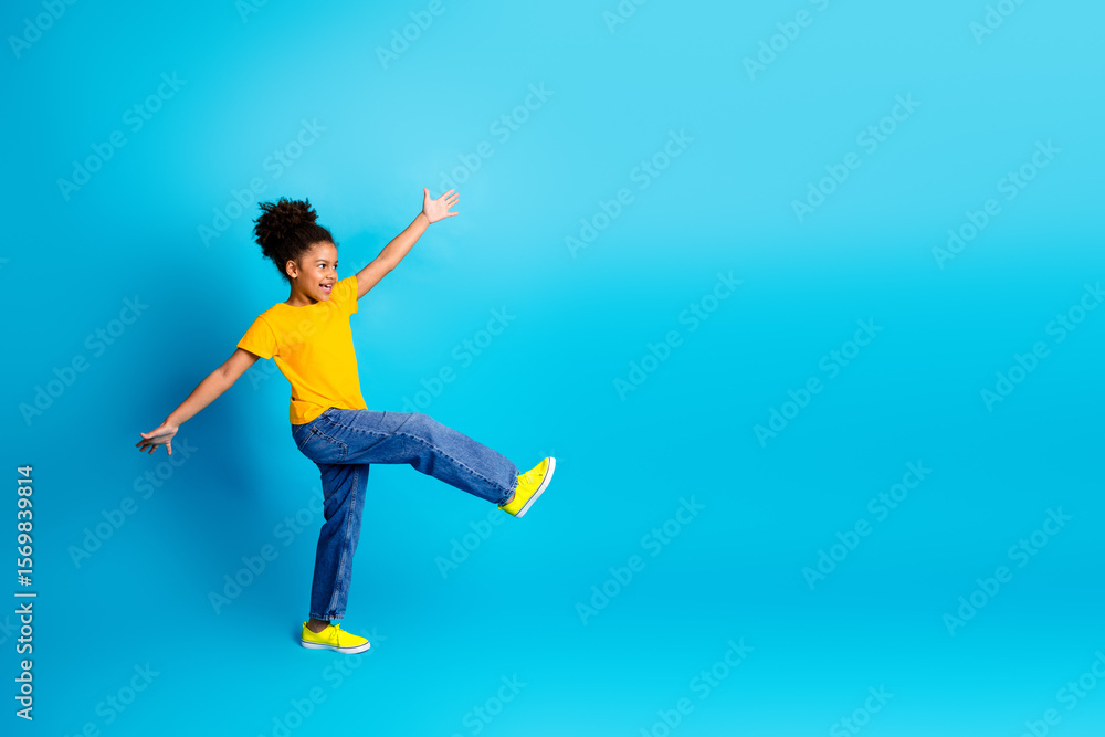 Fototapeta premium Cheerful young girl in casual outfit expressing joy against a vibrant blue background in a studio setting