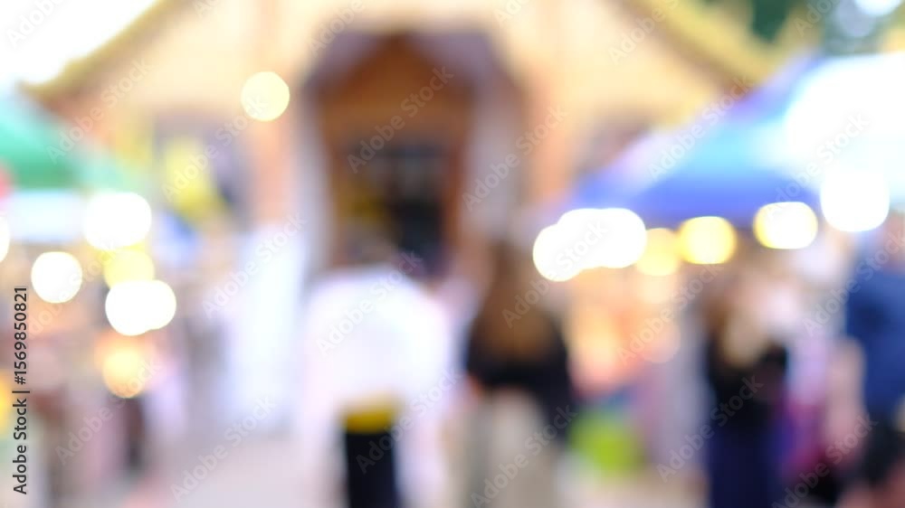 A blurry image of a crowded market with people walking around and umbrellas. Scene is busy and bustling, with people going about their day A blurry image of a crowded market with people walking around and umbrellas. Scene is busy and bustling, with people going about their day
