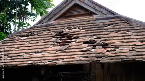 A roof with missing shingles and a hole in it. The roof is brown and has a wood frame