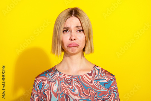 Young woman displaying a pouting expression in a bright yellow setting wearing a colorful patterned top