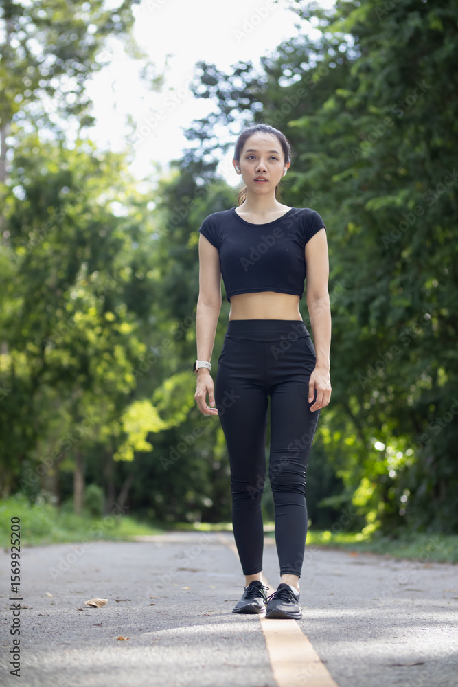 Portrait of a beautiful Asian woman in a black sportswear walking alone on the street after jogging in the morning. The athlete in a black is walking to warm up her body before jogging to get healthy. Portrait of a beautiful Asian woman in a black sportswear walking alone on the street after jogging in the morning. The athlete in a black is walking to warm up her body before jogging to get healthy.