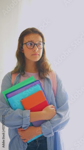 Wallpaper Mural Young student girl with glasses looking around uncertainly while holding study materials, perfect for back-to-school and adjustment scenarios Torontodigital.ca