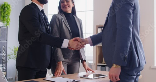 Smiling realtor shaking hands with young family couple, congratulating them with property purchase. Happy clients exchanging handshake with real estate agent after making successful deal in office.