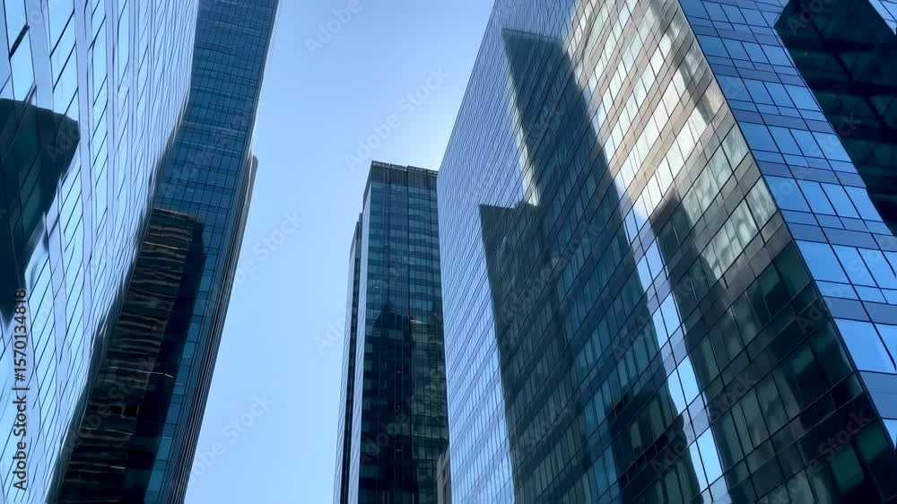 A cinematic low-angle shot of modern skyscrapers under a bright blue sky, glass buildings reflecting sunlight, slight lens flare, camera slowly tilting upward A cinematic low-angle shot of modern skyscrapers under a bright blue sky, glass buildings reflecting sunlight, slight lens flare, camera slowly tilting upward