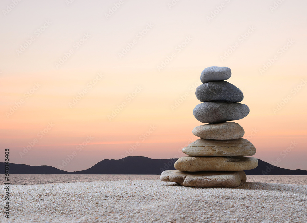 Fototapeta premium Stacked stones in a pyramid shape on a background of sea, mountains and sunset, copy space for design in your work, travel or zen theme.