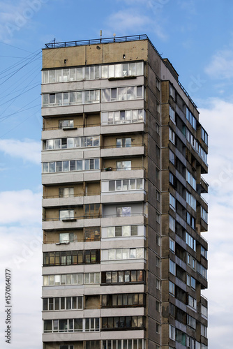 High-rise apartment building with aged concrete facade and enclosed balconies, reflecting Soviet-era architecture under a partly cloudy sky.