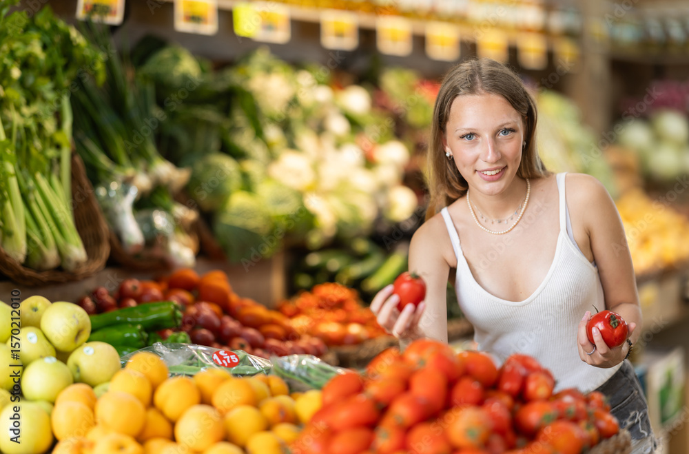Young woman shopping in vegetable store and buy tomato. Customer carefully examine goods, thinking about buying. Self-service store, vegetables and fruits from all over world. Young woman shopping in vegetable store and buy tomato. Customer carefully examine goods, thinking about buying. Self-service store, vegetables and fruits from all over world.