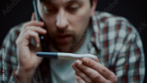A young man sits at home, holding a pregnancy test and talking on the phone. He looks frustrated and upset, discussing another failed attempt to conceive and sharing his disappointment
