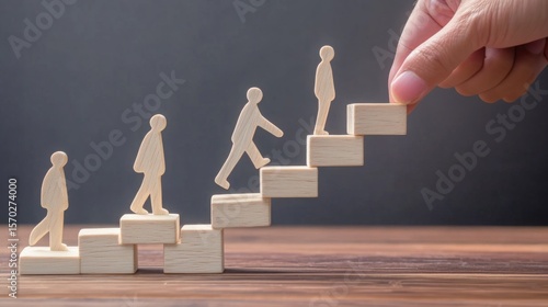 Wooden figures ascend stairs made of blocks, symbolizing growth, progress, and support, with a hand placing the final step.