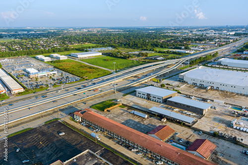 Complex multi level highway intersection with industrial warehouses, parking lots, surrounding suburban landscape in Houston, Harris County, Texas.