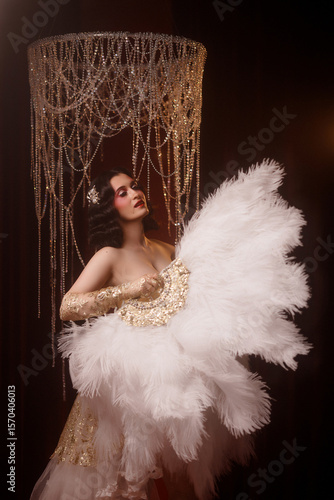 Wallpaper Mural Young Caucasian circus performer or burlesque dancer in golden vintage corset, front view, posing under chandelier on dark background. Concepts: circus, cabaret, retro, show, performance. Torontodigital.ca