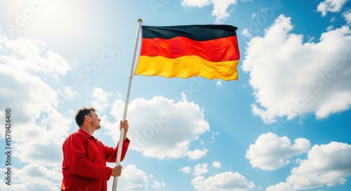 Man holding a large German flag against a blue sky with clouds