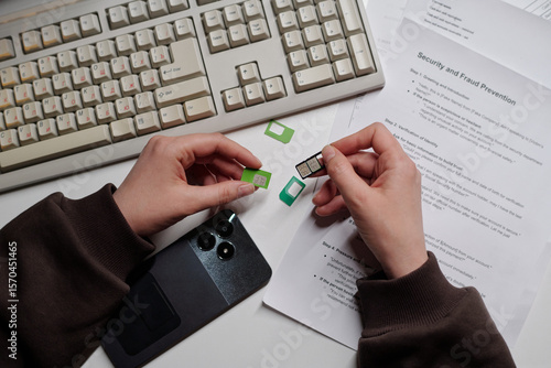 Woman holding SIM card and adapter near smartphone and documents, preparing device at desk, illustrating scam call center activity