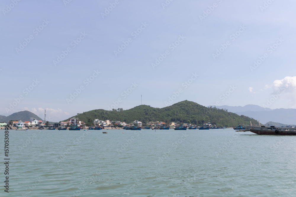 A calm sea with fishing boats at the base of lush green hills under a clear sky. A calm sea with fishing boats at the base of lush green hills under a clear sky.