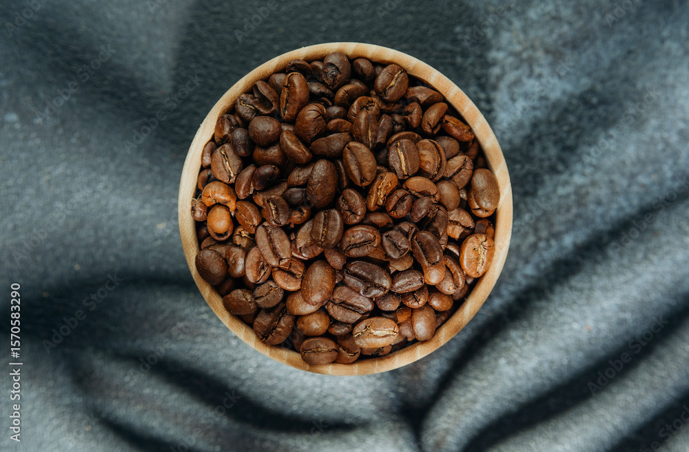 Fototapeta premium Coffee beans in wooden bowl with leaf shadow on dark background