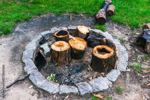Fototapeta Rustic round stone fire pit surrounded by freshly cut tree logs and firewood on a grassy campground