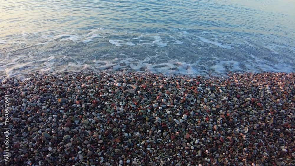 4K Close-up of gentle waves with a sound washing over colorful pebbled beach shore at Konyaalti in Antalya, Turkey. The clear Mediterranean water calmly meets the shoreline in the early morning light