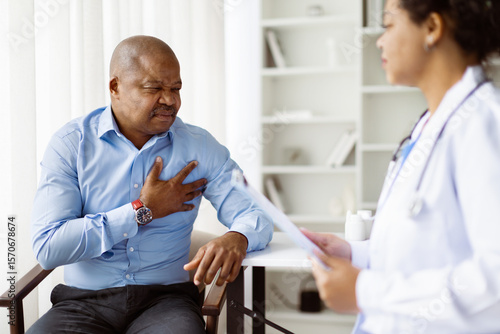 Male patient holding his chest in visible pain while talking with female doctor, possibly indicating a serious medical issue during consultation, closeup