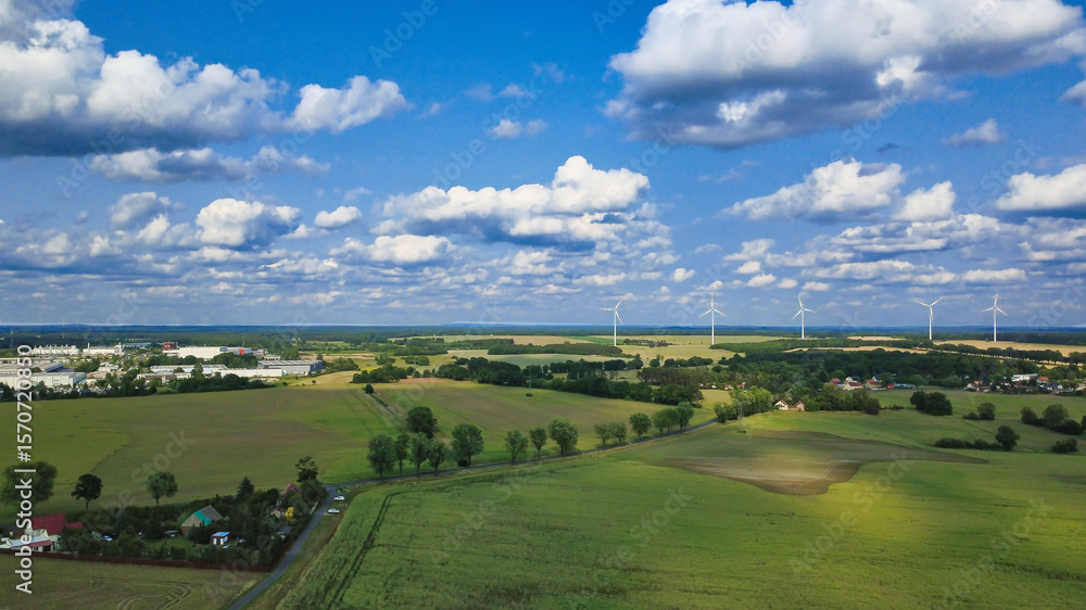 Obraz premium Vast agricultural landscape with wind turbines under a blue sky.