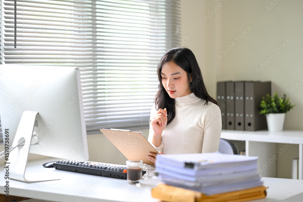 Smiling Asian businesswoman working at desk, reviewing documents during a video call Smiling Asian businesswoman working at desk, reviewing documents during a video call