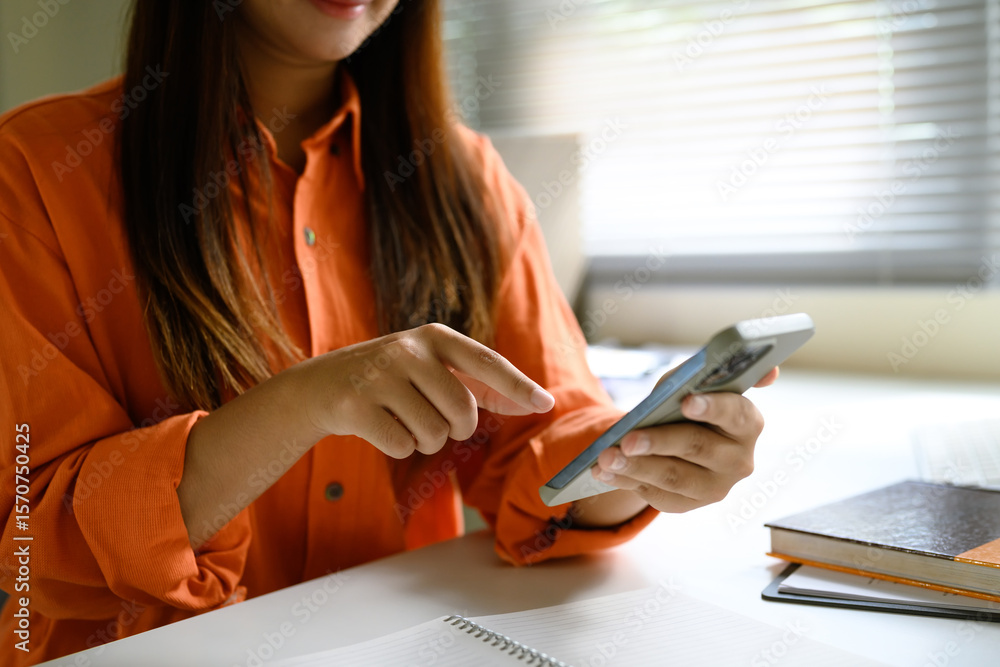 Fototapeta premium Close up of woman wearing an orange shirt using a smartphone at her desk