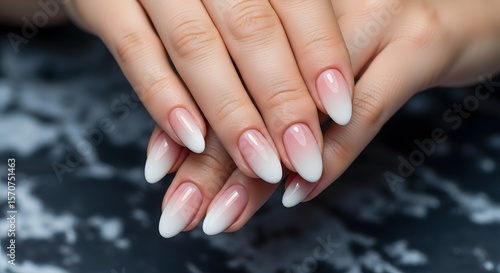 Close-up of elegantly manicured hands showcasing a soft ombre nail design, transitioning from white to pale pink on almond-shaped nails.