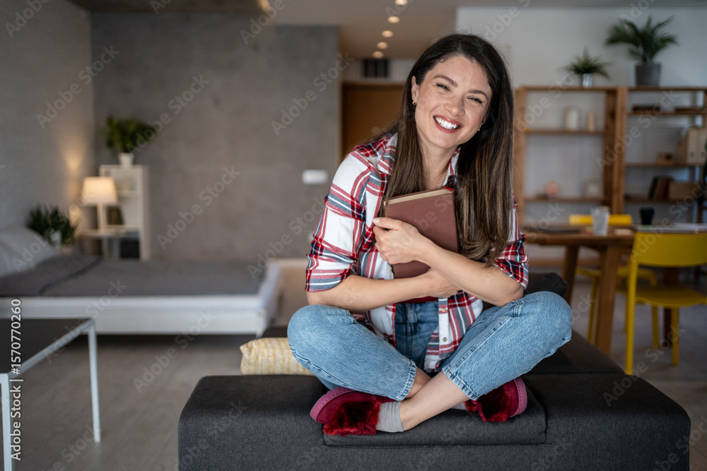 Obraz premium Happy woman hugging a book while relaxing on sofa at home